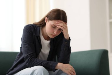 Evdeki kanepede oturan üzgün genç kadın.