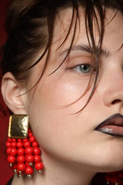 Siyah dudak kalemi olan güzel bir kadın koyu kırmızı arka planda şık küpeler takıyor.