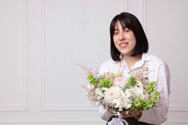 Beyaz duvarın yanında çiçeklerle dolu güzel bir çiçek buketi olan bir çiçekçi.