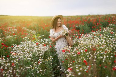 Bir çanta papatya çiçeğiyle gülümseyen kadın çayırda yürüyor.