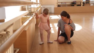 Gülümseyen bale öğretmeni dans sınıfında küçük bir kızla çalışıyor.