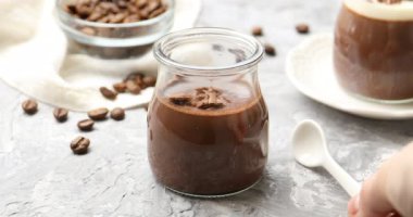 Gri desenli masadaki kavanozdan lezzetli çikolatalı panna cotta alan kadın, yakın plan.