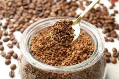 Kaşık granüle hazır kahve ve kavanoz beyaz masada, yakın plan.