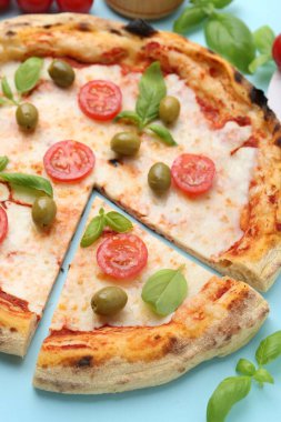 Açık mavi arka planda domatesli, fesleğenli ve zeytinli pizza, yakın plan.