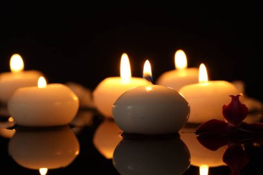 Yanan mumlar ve orkide çiçekleri ayna masasında siyah arkaplana karşı, yakın plan