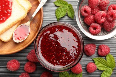 Cam kavanozda tatlı ahududu reçeli. Koyu gri ahşap masada böğürtlen ve ekmek dilimleri.