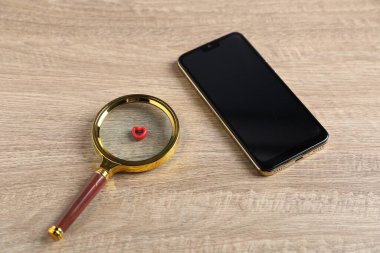 Online flört sitesi. Akıllı telefon, kırmızı kalp ve büyüteç ahşap masanın üstünde.