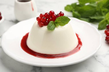 Kırmızı üzümlü lezzetli panna cotta, beyaz mermer masada sos ve nane, yakın plan.
