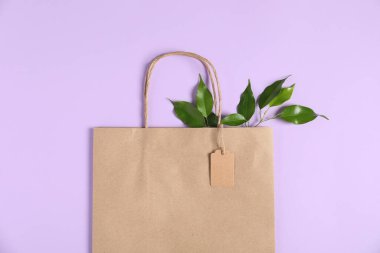Çevre dostu ambalaj. Karton etiketli kağıt çanta ve menekşe arkaplanda yapraklar, üst görünüm
