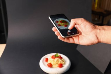 Adam stüdyoda akıllı telefonlu makarna fotoğrafı çekiyor, yakın plan. Profesyonel yemek fotoğrafçılığı.