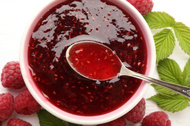 Tatlı ahududu reçeli kasede, böğürtlen ve yeşil yapraklar beyaz masada, düz yerde