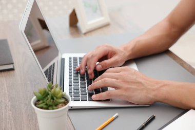 Kapalı alandaki ahşap masada dizüstü bilgisayar kullanan metin yazarı