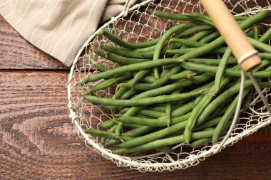 Beyaz sepet içinde taze bezelye kabukları ve ahşap masa üzerinde kumaş, üst görünüm