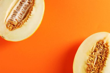 Turuncu arka planda olgun kavun yarımları, düz uzanmış. Metin için boşluk