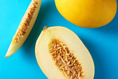 Açık mavi arka planda olgun kavunların tamamı ve kesimi düzdü.