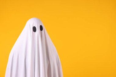Ürkütücü hayalet. Turuncu arka planda beyaz çarşaflı bir adam. Metin için boşluk