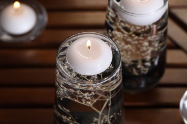 Mumlar ve çiçekler, su bardaklarında, ahşap masada, yakın plan.