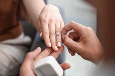 Evlenme teklif ediyorum. Adam içeride kız arkadaşının parmağına nişan yüzüğü takıyor.