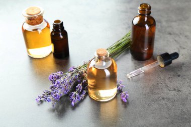 Şişelerdeki yağlar, lavanta çiçekleri ve gri desenli masadaki damlalar, yakın plan.