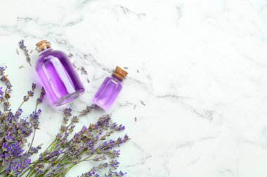 Aromatik esanslı yağ şişelerde ve lavanta çiçekleri beyaz mermer masada, düz yerde. Metin için boşluk
