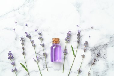 Beyaz mermer sehpanın üzerinde lavanta çiçekleri ve şişede yassı yağ var.