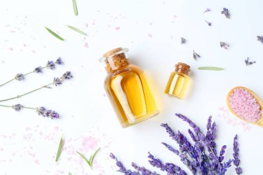 Şişelerdeki yağlar, lavanta çiçekleri ve beyaz masada deniz tuzu.