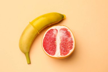 Seks eğitimi. Kondomlu muz ve bej arka planda yarım greyfurt, düz konum