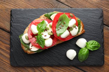 Peynirli, domatesli, ahşap masadaki fesleğenli lezzetli sandviç.