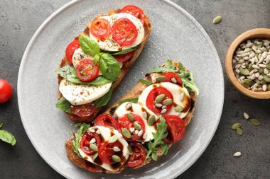 Mozarella peynirli lezzetli sandviçler ve gri masada domatesler.