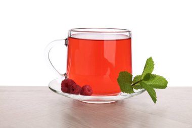 Aromatik ahududu çayı cam fincanda, böğürtlen ve yeşil yapraklar ahşap masada beyaz arka planda