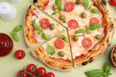 Açık yeşil arka planda leziz kesilmiş pizza ve malzemeler.