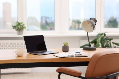 Modern dizüstü bilgisayarı ve ahşap masa üzerindeki kırtasiyesi olan şık bir iş yeri.