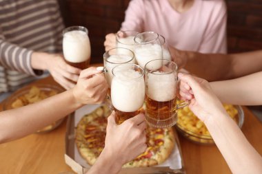 Bir grup arkadaş masa içinde bira bardaklarını tokuşturuyor, yakın plan.