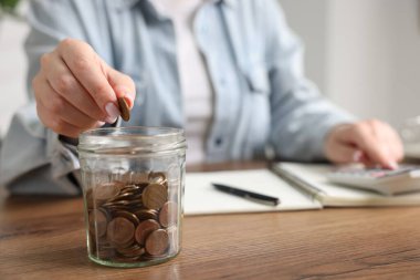 Ahşap masada paraları sayıp kavanoza koyan kadın, seçici odaklanma