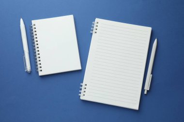 Mavi zemin üzerinde beyaz defterler ve kalemler, düz yatıyordu