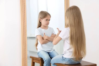Aynanın önünde baş parmağını gösteren küçük bir kız yansıması içeride gücenmiş yüz ifadesi sergiliyor. Bastırılmış duygular