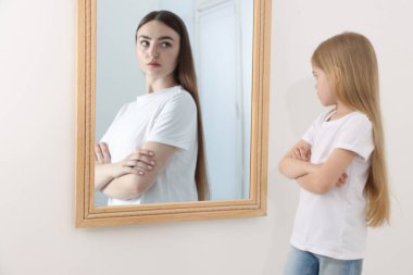 Küçük kız kendini aynada genç bir kadın olarak görüyor. Geçmiş ve gelecek hakkında kavramsal kolaj, zaman akışı, yaş