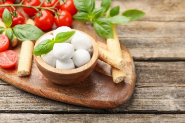 Lezzetli mozzarella peyniri topları, domatesler, fesleğen ve grissini ahşap masada, yakın plan. Metin için boşluk