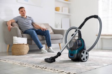 Evdeki kanepede dinlenen adam, elektrik süpürgesine odaklan.