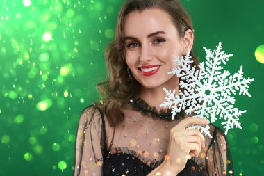 Mükemmel makyajlı gülümseyen kadın yeşil arka planda dekoratif kar taneleri tutuyor.