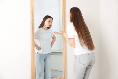 Heyecanlı bir kadın, aynada kendini rahatsız eden yansımasına bakıyor. Bastırılmış duygular