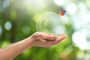 Kelebek kristal kürede oturan kadının ellerinde bulanık yeşil arka plan, yakın plan