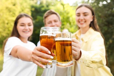 Bir grup mutlu arkadaş açık havada bira bardakları tokuşturuyor, seçici odaklanma.