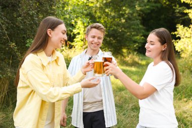 Bir grup mutlu arkadaş dışarıda bira bardaklarını tokuşturuyor.