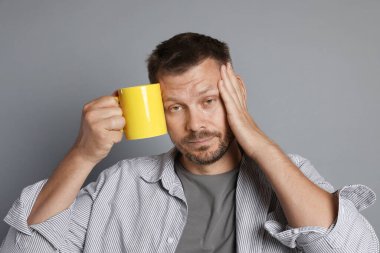 Gri arka planda içki mahmurluğu çeken bir adam.