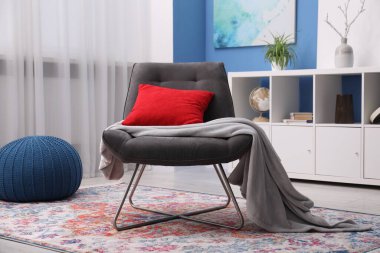 Oturma odasında kırmızı yastıklı ve battaniyeli rahat gri koltuk. İç tasarım