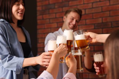 Bir grup mutlu arkadaş masanın içinde bira bardaklarını tokuşturuyor, seçici bir odak noktası var.