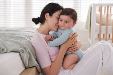 Anne, küçük bebeğini evin içinde yatağın yanına koymuş.