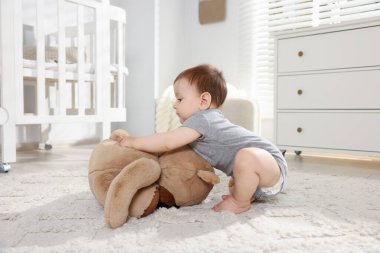 Küçük şirin bebek odada oyuncak ayıyla oynuyor.