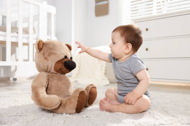 Küçük şirin bebek odada oyuncak ayıyla oynuyor.